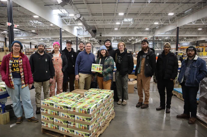 Team of employees posing together in a spacious warehouse with neatly arranged pallets of packaged goods.