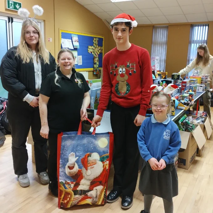 Group of people in a room with Christmas decorations, one holding a festive Santa-themed gift bag.