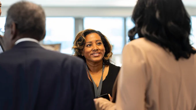 Kenyatta Hazlewood faces the camera, smiling, while speaking to two people.