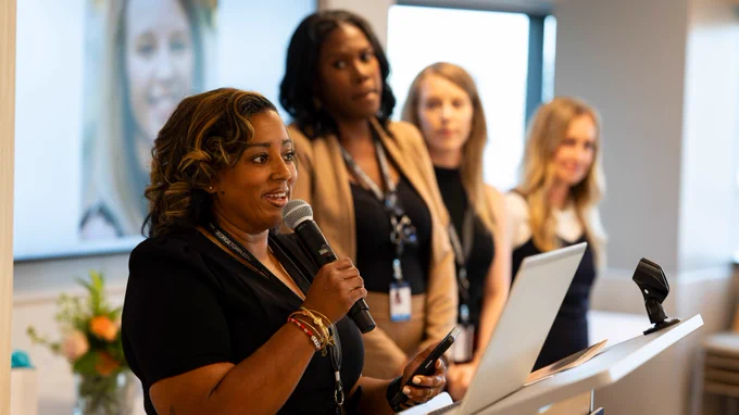 Kenyatta speaks at a podium with members of her nursing cohort behind her.