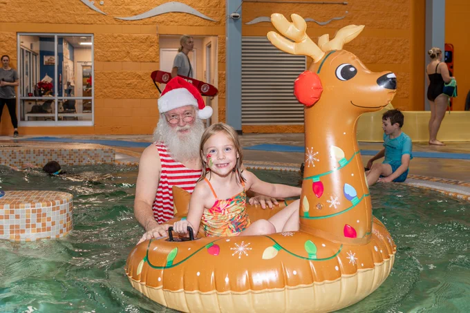 Santa pushes a young girl in an inflatable reindeer innertube in an indoor swimming pool 