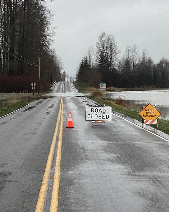 Road Closed and Water Over Roadway signs leading into Silvana. Pooling water is visible in the background.
