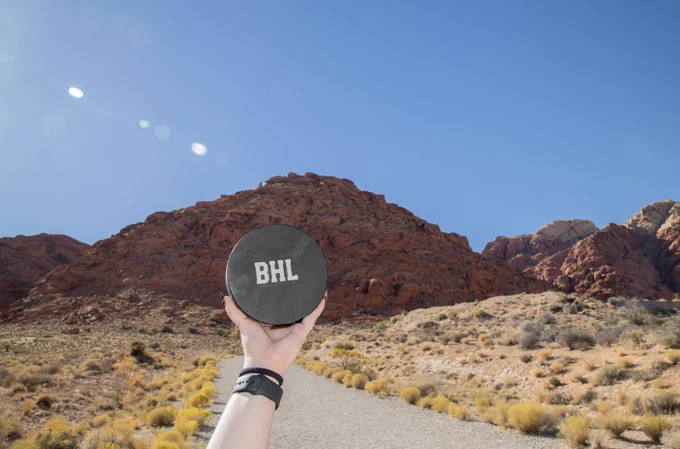 An extended arm holding the blind hockey puck with the BHL logo with the desert sand hill in the background.