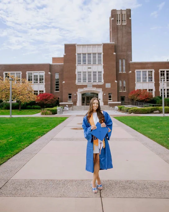 Boise State student wearing undergraduate regalia and smiling in front of the Administration Building.
