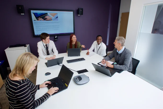 Five people are sitting around a table with laptops