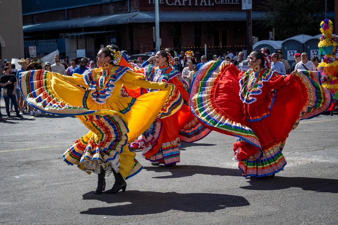 Folklorico dancers swirl their colorful skirts in an outdoor parade performance.