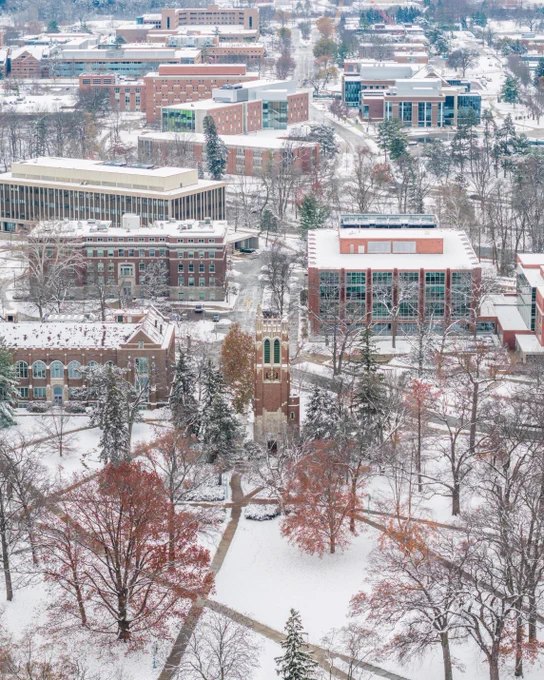 Aerial shot of a snow-covered university campus. The scene features brick buildings and snow-laden trees. Beaumont stands amid the winter landscape. Roads and walkways are also covered with snow.