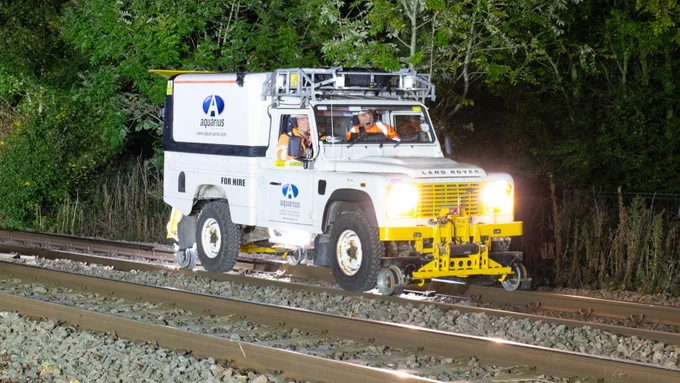 A photograph of an adapted Land Rover on the railway tracks with two rail workers inside.