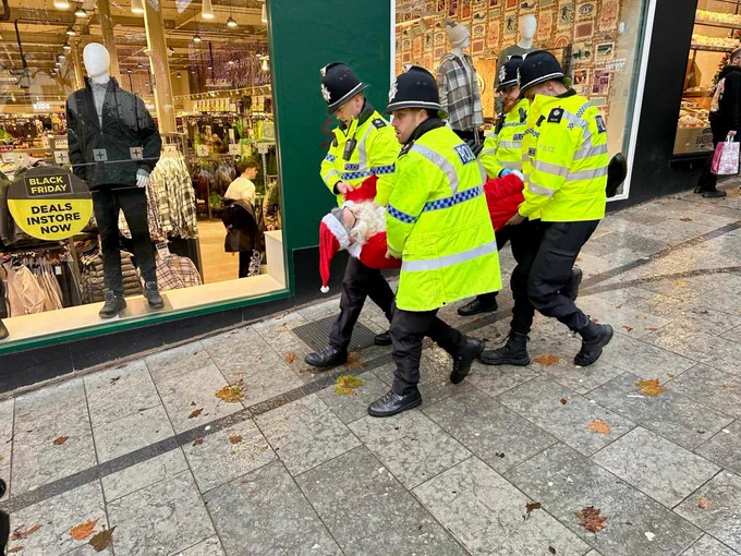 An image of four policemen carrying an arrested Santa Claus down a street.