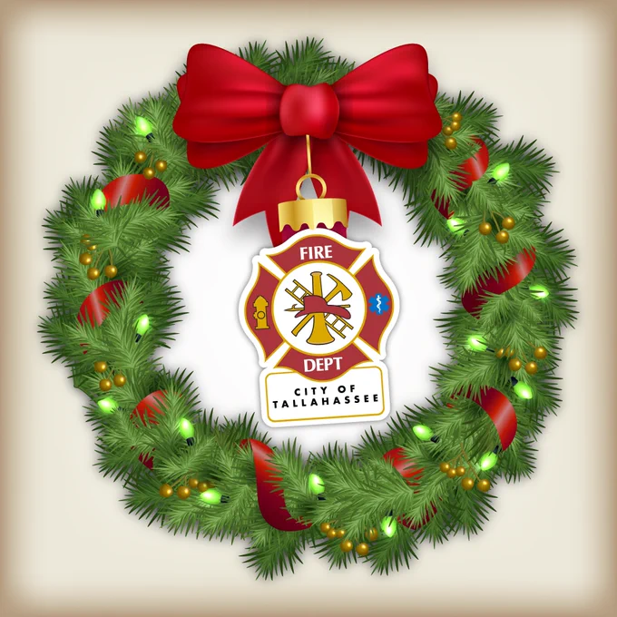 Holiday wreath decorated with green lights and a large red bow, featuring a central badge representing the City of Tallahassee Fire Department.