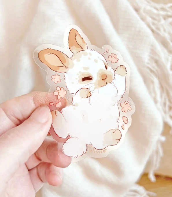 A hand holding a vinyl sticker of a cute, sleeping bunny with a clear background.