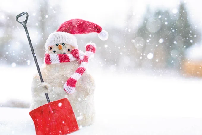 Charming snowman wearing a Santa hat and scarf with a red shovel in a snowy setting.