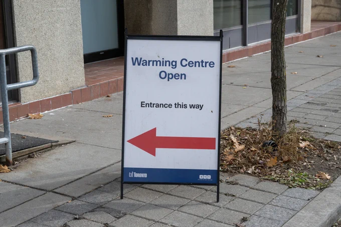 Sign on sidewalk that says 'Warming Centre Open' with directional arrow. 