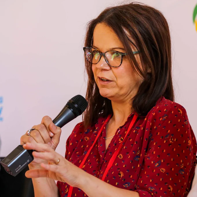 Joan Condell in a red patterned blouse speaking into a microphone during an event.