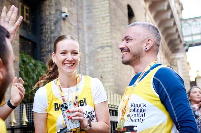 Two runners wearing yellow King's College Hospital Charity vests chatting outdoors near a brick building after the London Landmarks Half Marathon
