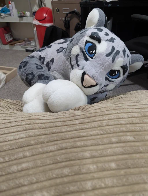 A plush snow leopard resting her paws on a bean bag looking up at you