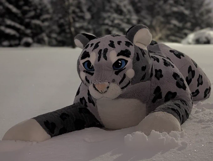 A plush snow leopard resting in the snow