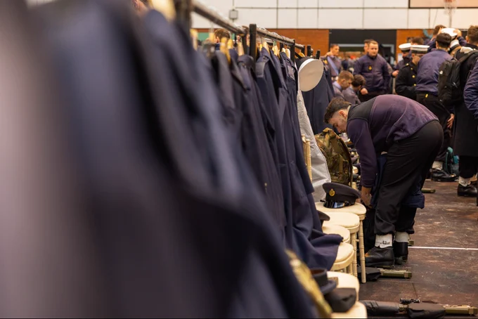 A sailor dresses in his uniform in the changing rooms at Victoria Barracks, coats line the walls on hangars