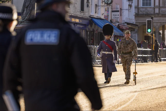 The guards sector commanders chalk out the processional route in Windsor High Street for the street liners using a measuring wheel. A policeman watches on