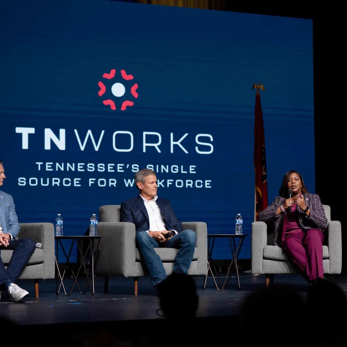 Three panelists on stage at a TNWorks event, with one panelist speaking and the others listening, including Tennessee Governor Bill Lee, in front of a backdrop displaying the TNWorks logo.