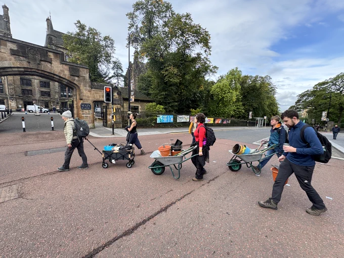 A group of people pushing wheelbarrows filled with excavation equipment across University Avenue 