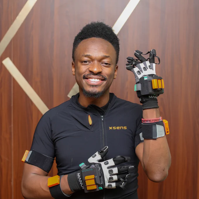 2025 Africa Prize winner Elly Savatia wearing a black T-shirt and equipped with advanced Xsens motion capture gloves smiles at the camera.