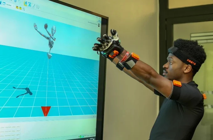 2025 Africa Prize winner Elly Savatia using a wearable robotic glove to interact with a 3D simulation on a computer screen.