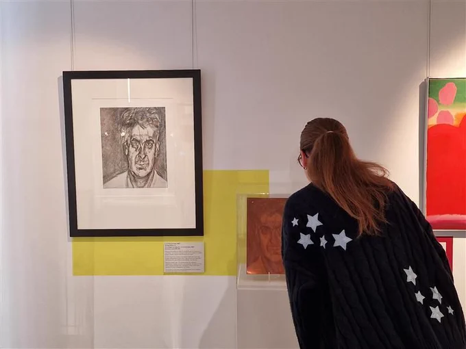 A woman with long, copper hair examines a portrait on the wall of a gallery. 