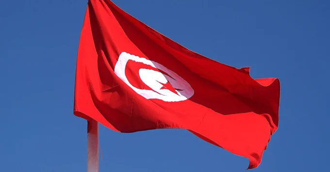 Le drapeau de la Tunisie flottant au vent sur un fond de ciel bleu.