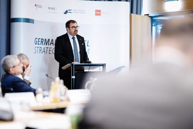 Florian Hahn steht an einem Rednerpult auf dem Germany-Israel Strategic Forum. Hinter ihm befindet sich ein großes Banner mit der Aufschrift „Germany-Israel Strategic Forum“. Vor dem Redner sitzen Teilnehmende an einem Konferenztisch.