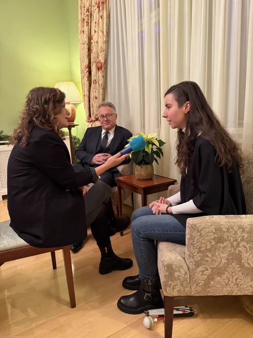 Youth Disability Advocate Mia interviewed by Mojca Delač from radio programme Prvi. They are sitting in the armchairs in the dining room at the Residence, joined by Chargé D’Affaires Nigel Baker.