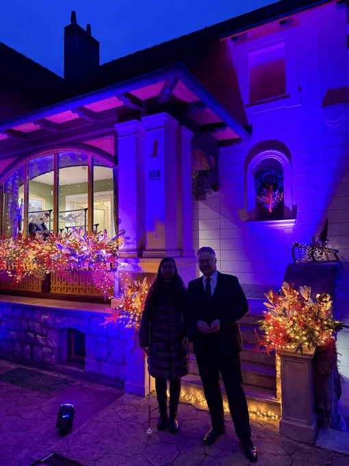 Chargé D’Affaires Nigel Baker and Youth Disability Advocate Mia in front of the Residence which is lit up in purple in honour of the International Day of Persons with Disabilities, and adorned with some Christmas decorations.