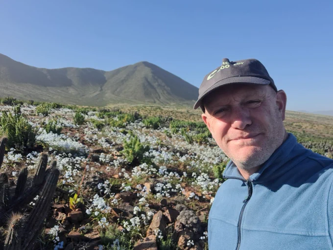 A man in a Chester Zoo cap and zipped up hoodie standing in a desert habitat