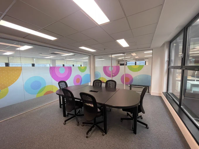 A modern conference room with a black oval table, six black chairs and colourful circular patterns on the glass walls.