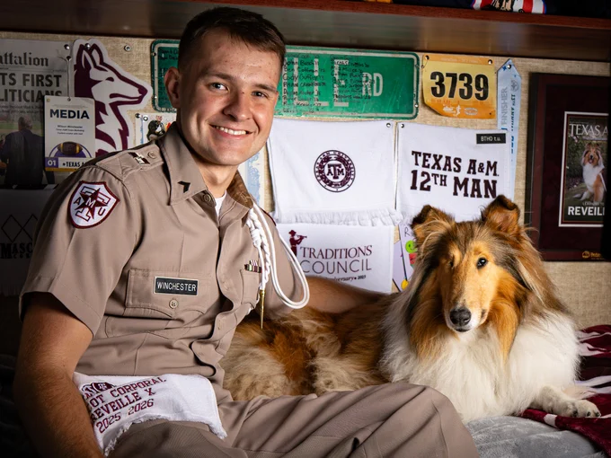 Person in Texas A&M University uniform sitting with a Collie dog, surrounded by banners and memorabilia.