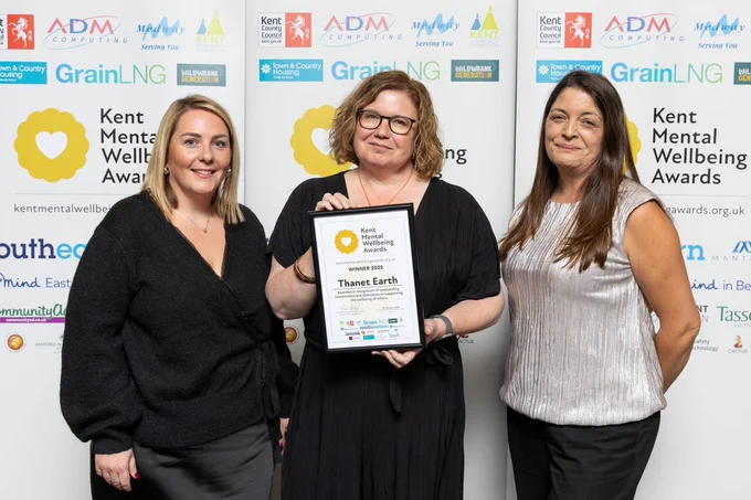 Three people are smiling and their winners certificate is being held aloft
