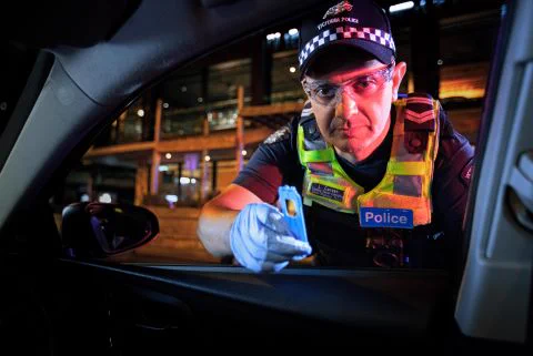 Victorian Police officer in full uniform leaning into a car windown holding a drug test in his gloved hand.