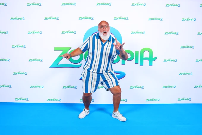 Picture of David Fane in a white and blue outfit posing in front of Zootopia 2 red carpet (although the carpet is blue)