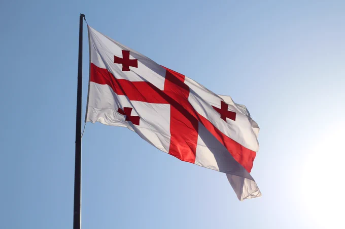 The flag of Georgia blowing in the wind against a light blue sky