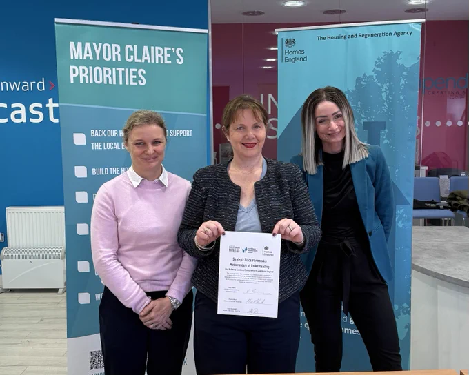 Amy Rees, Claire Ward and Amy Harhoff stand together smiling, holding a signed strategic place partnership document.