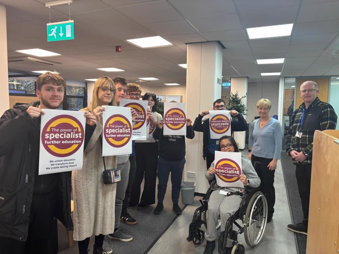 Clare with many learners and staff. The learners are all holding posters with "The Power of Specialist FE" campaign logo on them