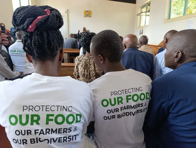 A group of people, many of whom are wearing shirts that say "Protecting our food, our farmers and our biodiversity." 