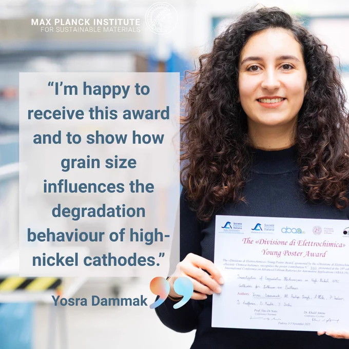 Person with curly hair holding a certificate. The background shows scientific devices.