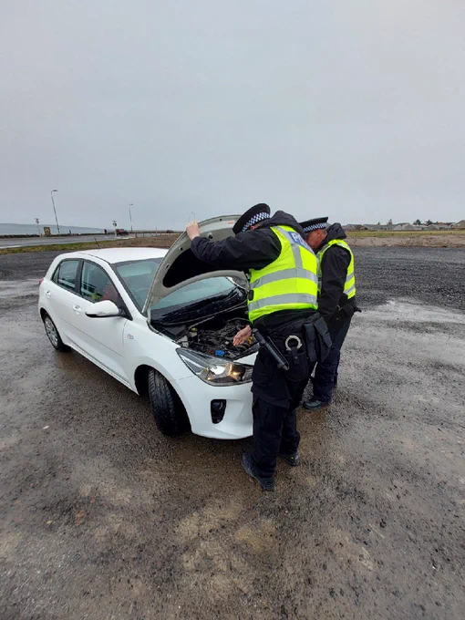 Uniformed officers check a white vehicle to ensure it is in a road worthy condition for winter conditions.