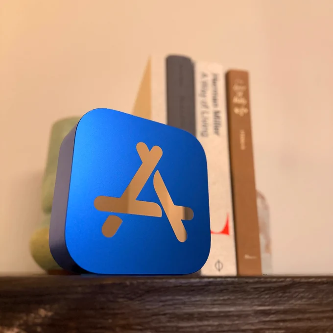 The App Store award, resembling the App Store app icon, sitting on a desk in front of some books.