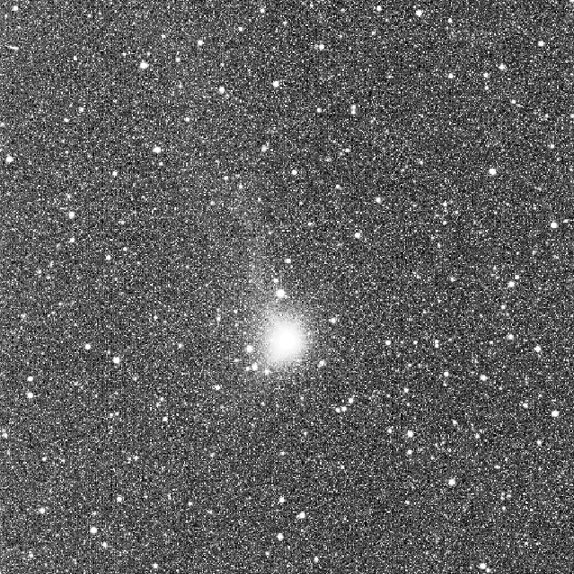 Grainy space image, with white dots on a dark background. At the centre of the image is a larger, bright white blob with a faint white line stretching towards the top of the frame.