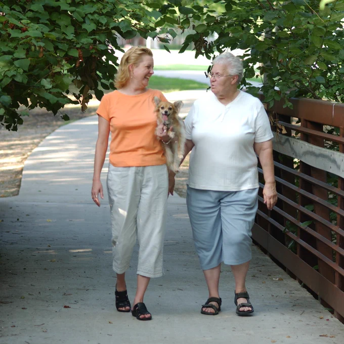 Two women walking on a paved trail. One woman is holding a dog.