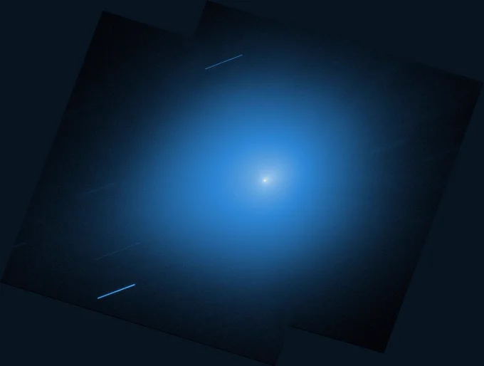 An image from NASA’s Hubble Space Telescope showing the interstellar comet 3I/ATLAS. The comet is a small white dot in the center of the image, with a light blue halo of light that takes up most of the image. Other stars are shown streaking across the image as diagonal blue-white lines.