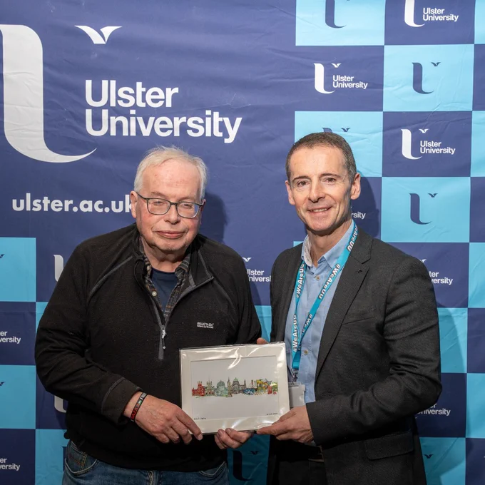 Dr Paul Darby of Ulster University photographed with Professor Alan Bairner, in front of an Ulster University backdrop.