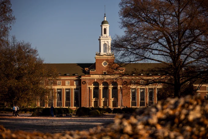 View of the Edmon Low Library at Oklahoma State University during sunset, highlighting its classic red brick facade and prominent white clock tower.